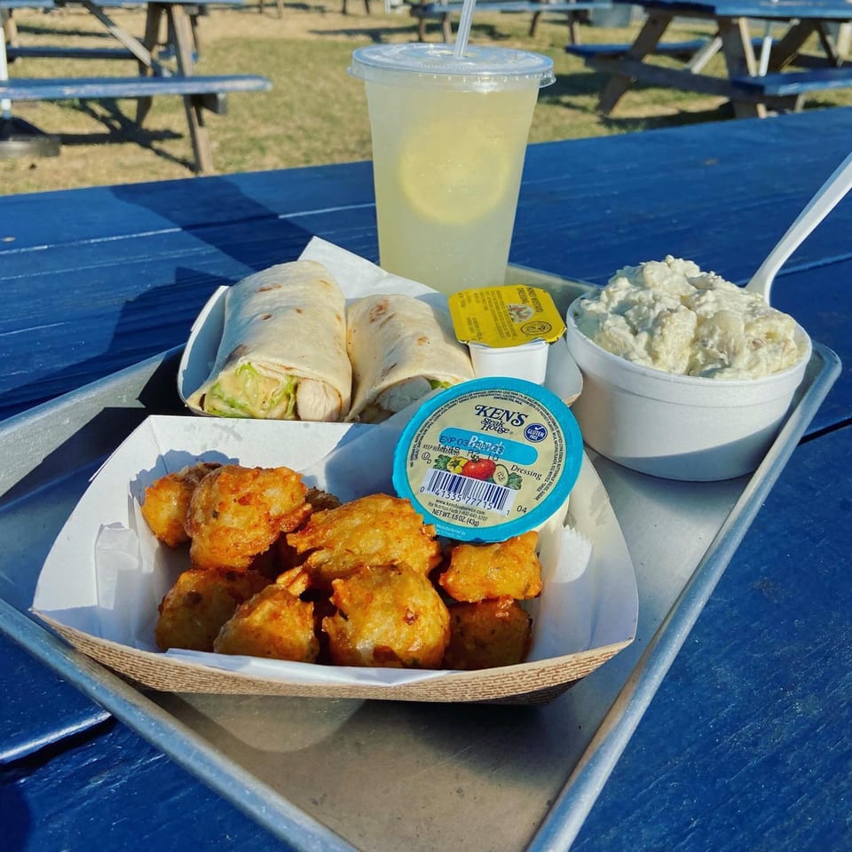 A tray with two wraps, potato salad, fried nuggets, and lemonade on a blue picnic table.