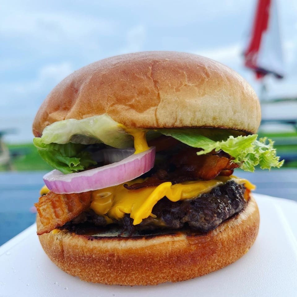 Close-up of a Sea Level burger with cheese, bacon, lettuce, and red onion on a bun.